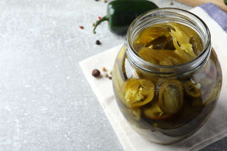 Glass jar with slices of pickled green jalapeno peppers on light gray table, space for text