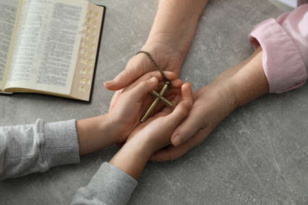 Boy and his godparent holding cross at gray table, closeupの写真素材