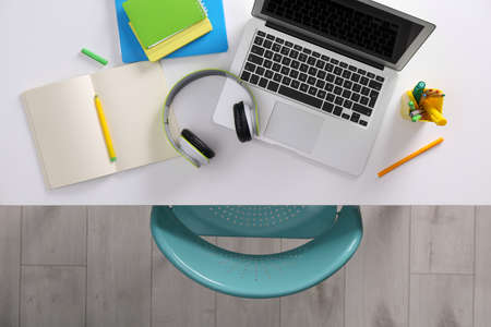 Chair near white table with laptop, headphones and stationery indoors, top viewの写真素材
