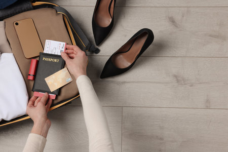 Woman packing suitcase on wooden floor, top view with space for text. business trip planning