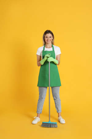 Young woman with broom on orange backgroundの写真素材