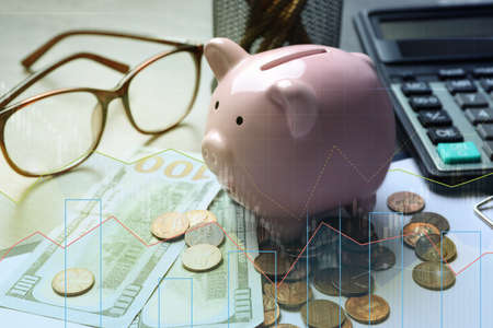 Pink piggy bank and money on table. illustration of financial graphsの写真素材