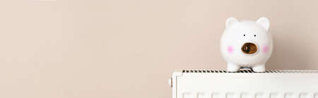 Piggy bank on heating radiator near light wall, space for text. banner designの写真素材