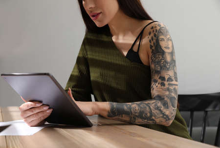 Beautiful woman with tattoos on arm using tablet at table indoors, closeupの写真素材