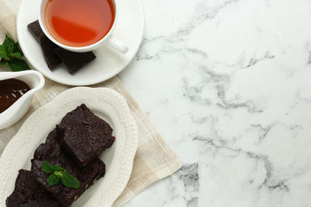 Delicious brownies served with tea and chocolate syrup on white marble table, flat lay. Space for textの写真素材