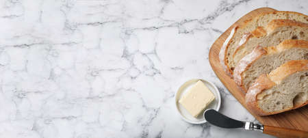 Freshly baked bread and butter on white marble table, flat lay with space for text. banner design