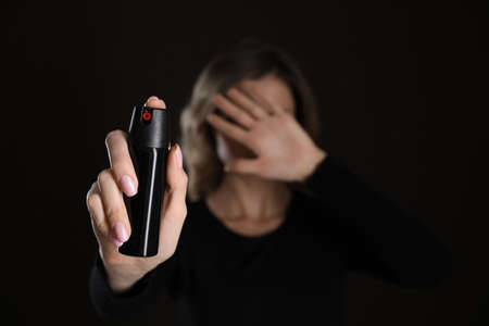 Young woman covering eyes with hand and using pepper spray on black background, focus on canister. Space for textの写真素材
