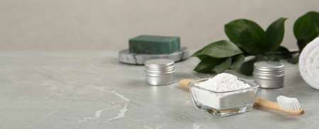 Composition with tooth powder and green leaves on light gray marble table, space for text. banner...