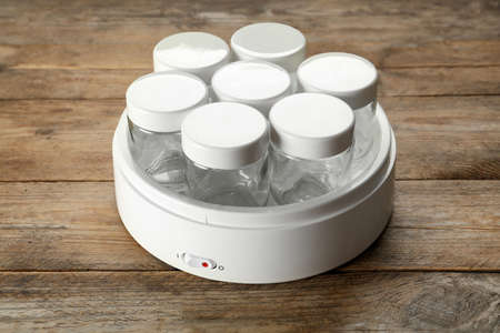 Modern yogurt maker with empty jars on wooden table
