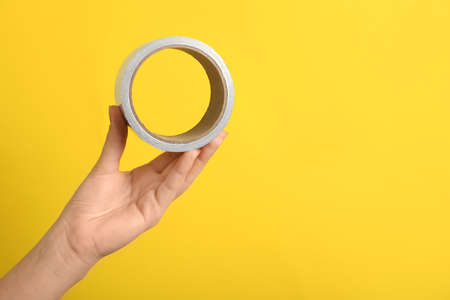 Woman holding adhesive tape on yellow background, closeup. Space for textの写真素材