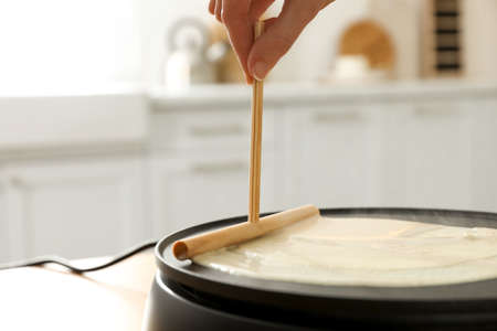 Woman cooking delicious crepe on electrical pancake maker in kitchen, closeupの写真素材