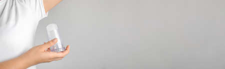 Young woman holding natural crystal alum deodorant near armpit on light gray background, closeup...
