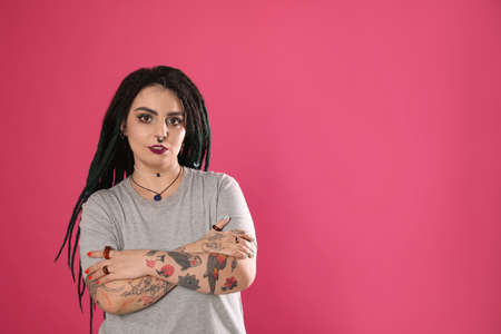 Beautiful young woman with tattoos on arms, nose piercing and dreadlocks against pink background....