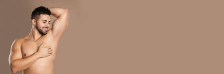 Young man showing armpit after applying deodorant on brown background, space for text. banner designの写真素材
