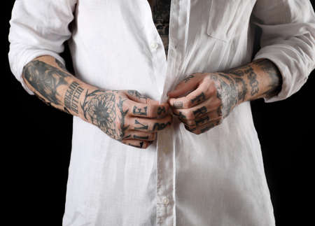 Young man with tattoos on body against black background, closeup