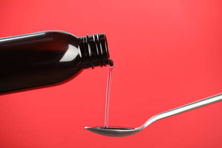 Pouring cough syrup into spoon on red backgroundの写真素材
