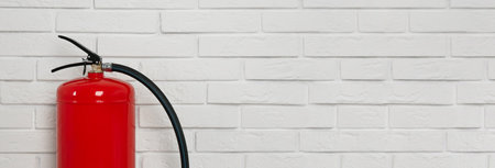 Fire extinguisher near white brick wall, space for text. banner design