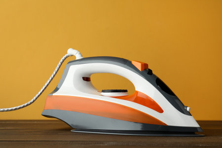One modern iron on wooden table against orange background. home appliancesの写真素材
