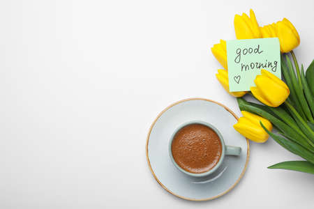 Cup of aromatic coffee, beautiful yellow tulips and Good Morning note on white background, flat lay....