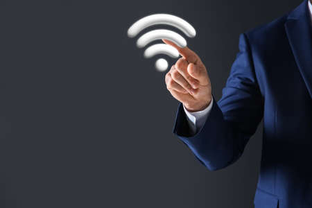 Man touching Wi Fi symbol on digital screen against dark gray background, closeupの写真素材