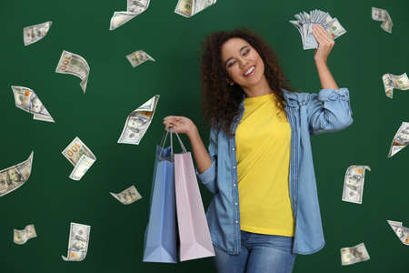 Happy young African American woman with shopping bags and money and falling American dollars on green backgroundの写真素材