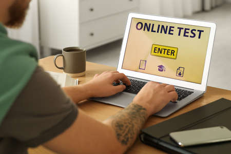 Man taking online test on laptop at desk indoors, closeupの写真素材