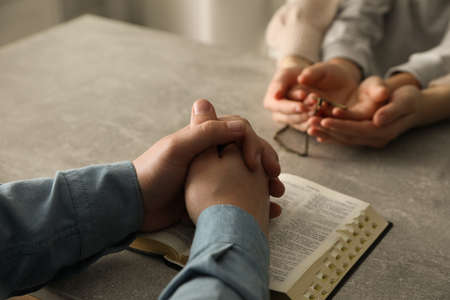Boy praying and reading Bible with his godparents at gray table indoors, closeup