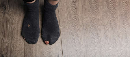 Poor person in shabby socks on wooden floor, closeup view with space for text. banner design