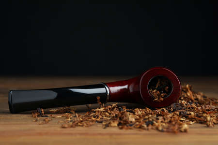 Smoking pipe and dry tobacco on wooden table against dark background. Space for textの写真素材