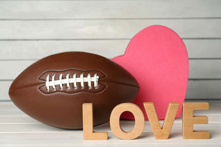 American football ball, heart and word Love on white wooden tableの写真素材