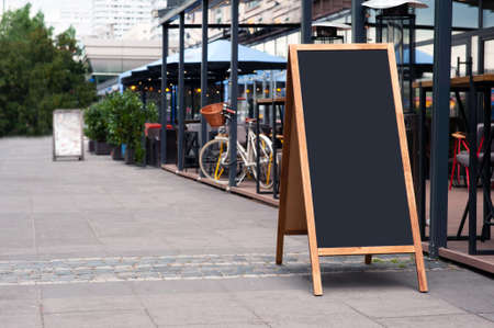 Blank wooden sandwich board near outdoor cafe. Mockup for design