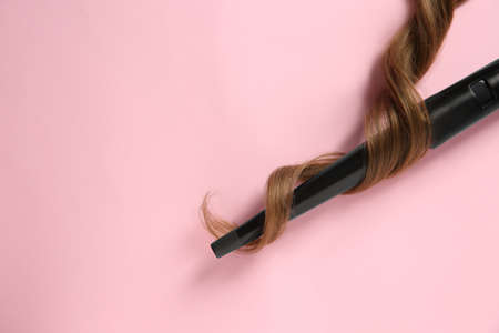 Modern clipless curling iron and brown hair lock on pink background, top view. Space for text