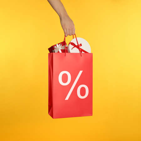 Woman holding paper shopping bag with percent sign on yellow background, closeup. discount concept