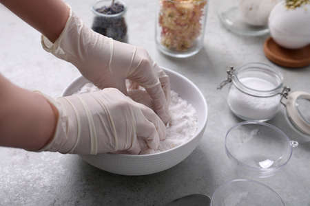 Woman in gloves making bath bomb mixture at gray table, closeup