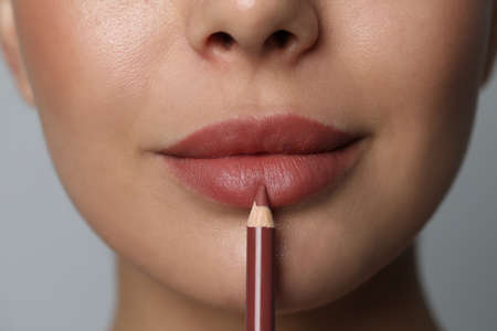 Young woman applying beautiful nude lip pencil on gray background, closeupの写真素材