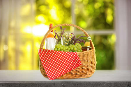 Picnic basket with flowers, wine and food on stone table indoors