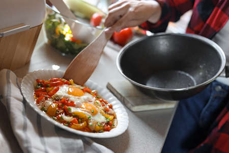 Woman freshly fried eggs with vegetables onto plate in kitchen, closeupの写真素材
