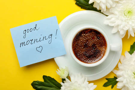 Cup of aromatic coffee, beautiful white chrysanthemums and Good Morning note on yellow background,...