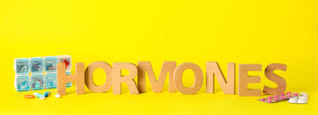 Word Hormones made of wooden letters and pills on yellow backgroundの写真素材