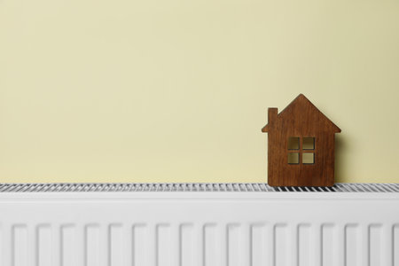 Wooden house model on heating radiator near beige wall, space for text. energy efficiency conceptの写真素材