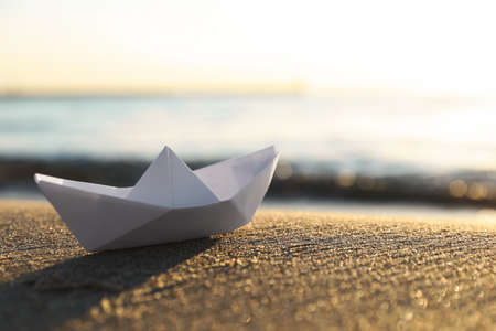 White paper boat on sand near sea at sunset, closeup. Space for textの写真素材