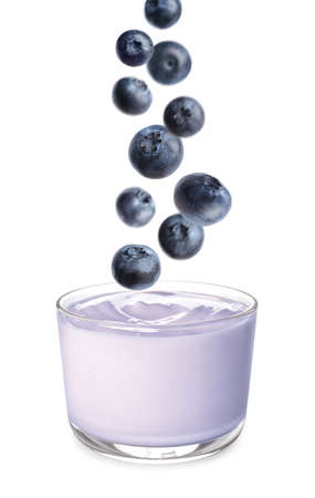 Many fresh blueberries falling into glass bowl of yogurt on white backgroundの写真素材