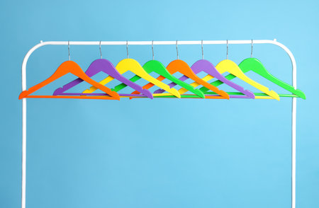 Bright clothes hangers on metal rack against light blue backgroundの写真素材