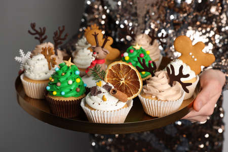 Woman holding tasty Christmas cupcakes on light background, closeupの写真素材