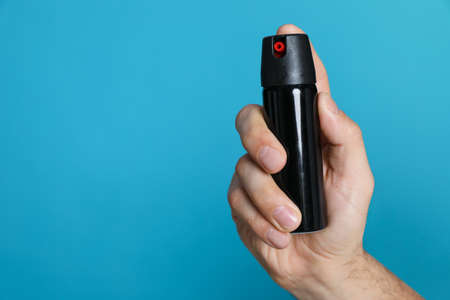 Man using pepper spray on turquoise background, closeup. Space for text