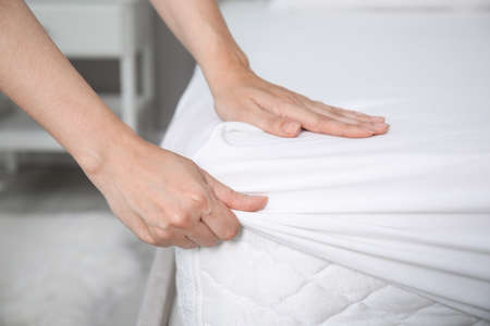 Woman white fitted sheet over mattress on bed indoors, closeup