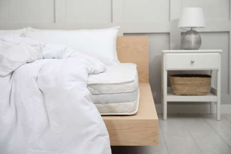 Wooden bed with soft white mattress, blanket and pillows indoorsの写真素材