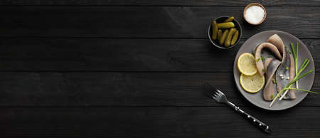 Salted herring fillets served with green onions and lemon on dark wooden table, flat lay with space for text. banner designの写真素材
