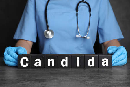 Doctor holding black cubes with word Candida at gray table, closeup