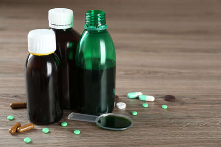 Bottles of cough syrup, dosing spoon and pills on wooden tableの写真素材